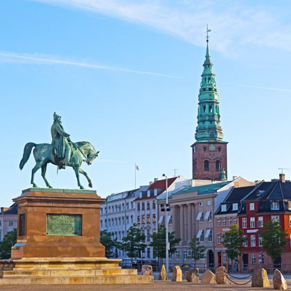 Rytterstatue på torg med fargerike bygninger og kirketårn i bakgrunnen