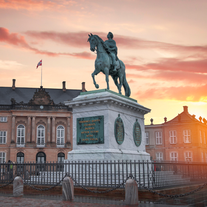 Rytterstatue på marmor­sokkel foran Amalienborg Slot ved solnedgang