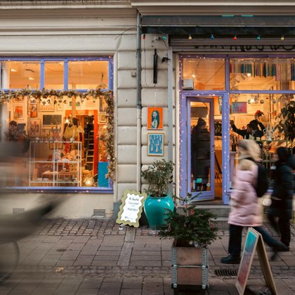 Colorful street-level shop with lit windows and a purple door, Christmas decorations in the window and people walking past on the sidewalk.