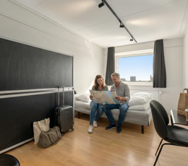 Two people sitting in a room with a double bed and desk