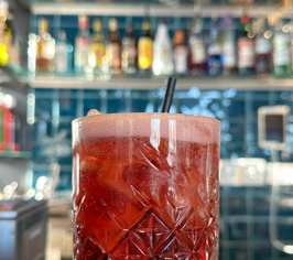Röd cocktail med is serverad i ett glas vid baren.